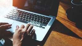 hands on a laptop keyboard, seated at a table.